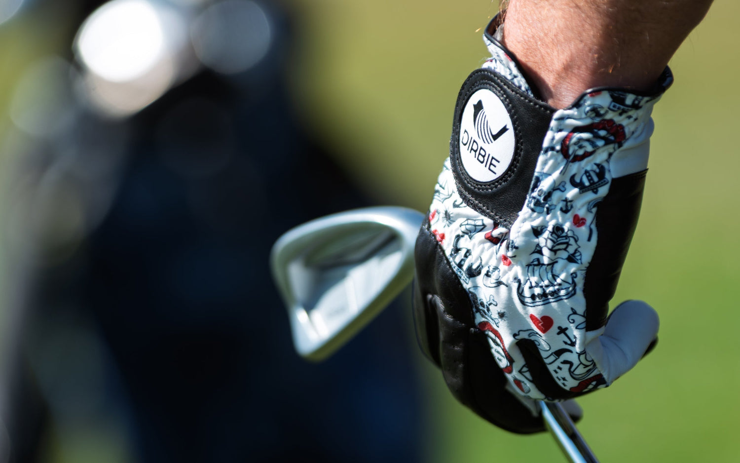 Which hand to wear a golf glove on? A Dirbie golf glove holding a golf club infront of a golf bag. 